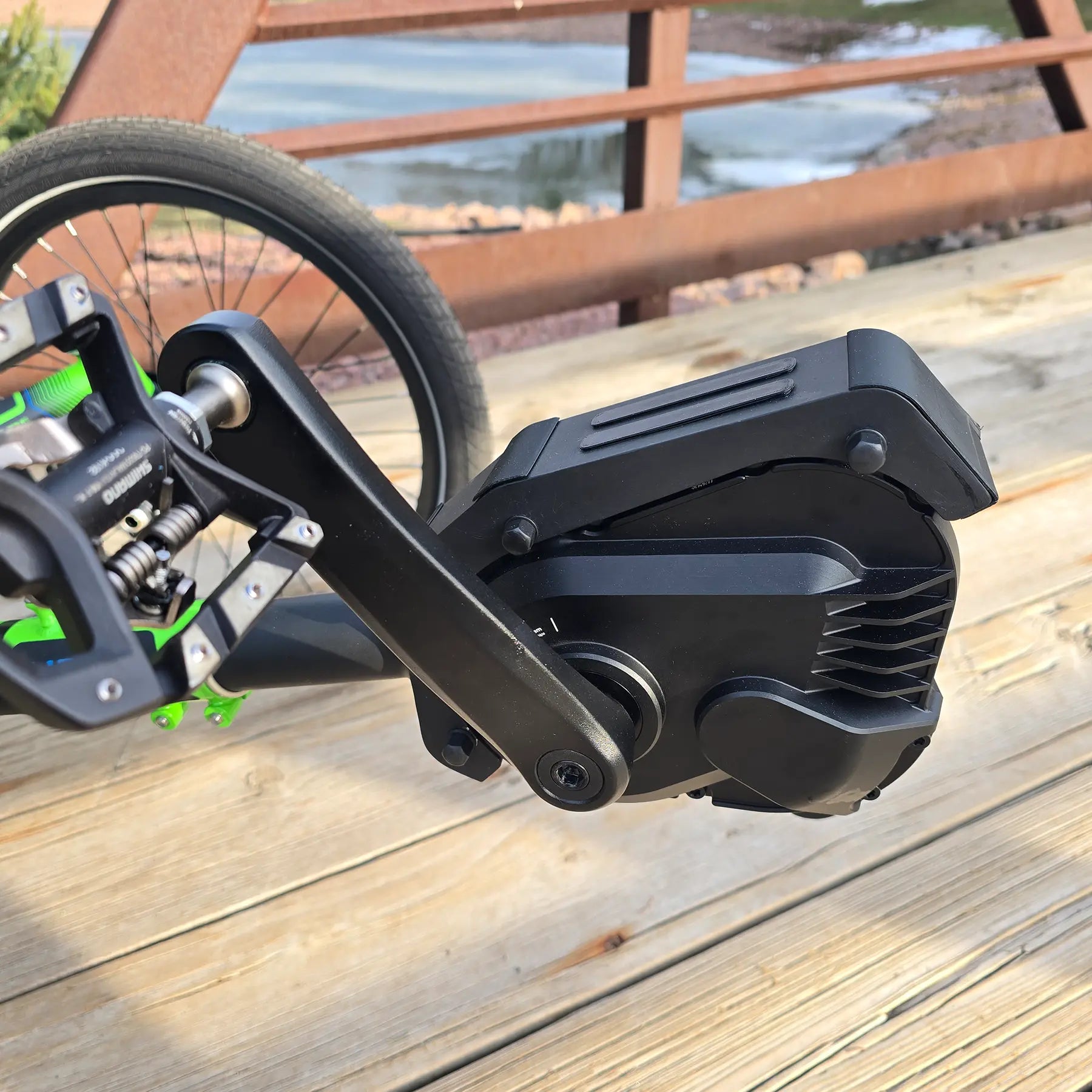 Closeup view of pedals and motor on the ICE Adventure HD 26 FS PERS Chainless Kiwi Green Recumbent Trike on a bike path near a melting pond.