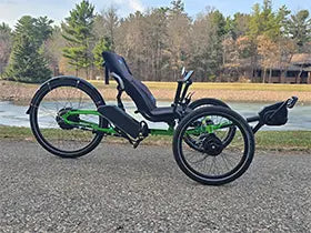 The ICE Adventure HD 26 FS PERS Chainless Kiwi Green Recumbent Trike on a bike path alongside a melting pond with trees in the background.