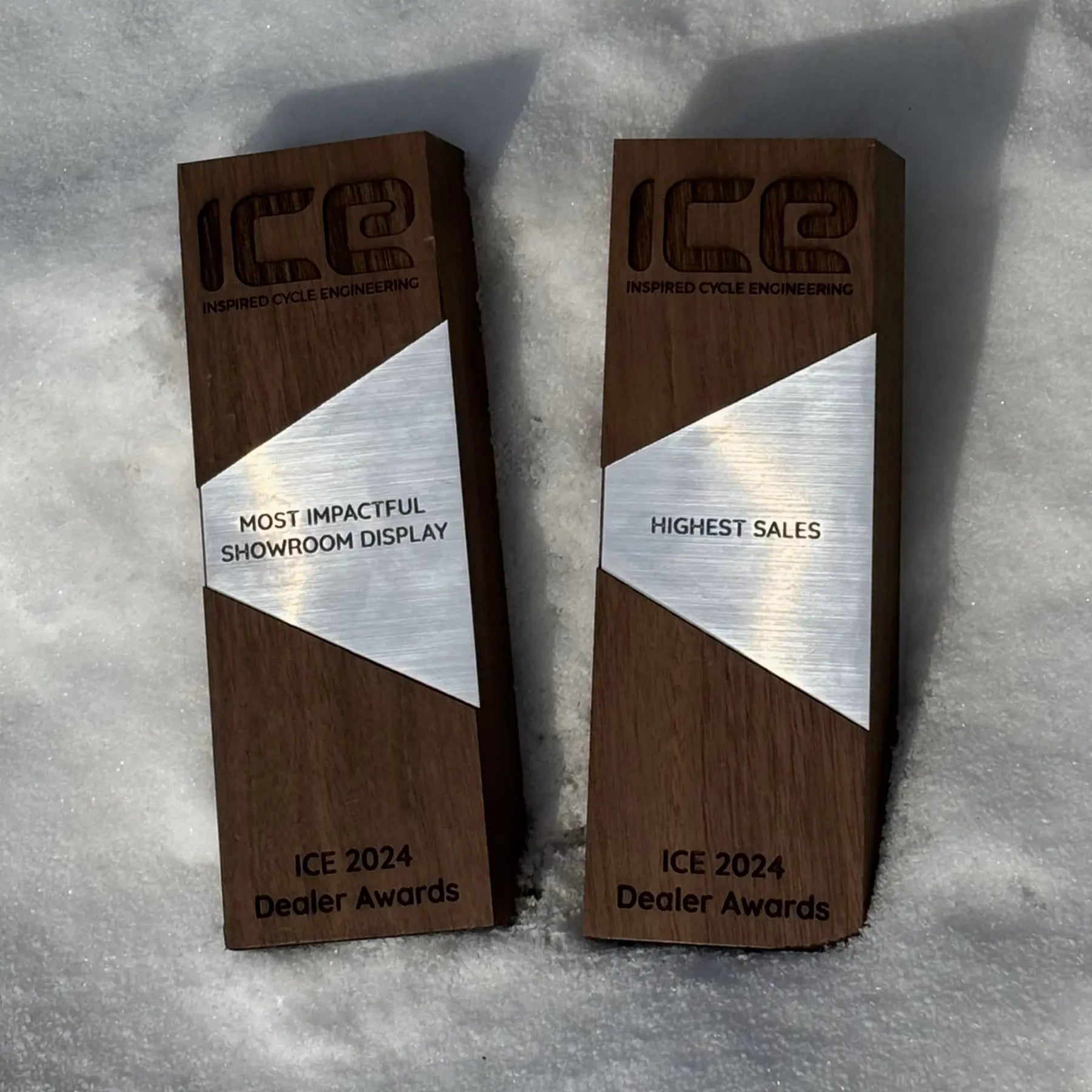Two wooden awards with silver accents on a textured surface, featuring text indicating 'ICE 2024 Dealer Awards'.