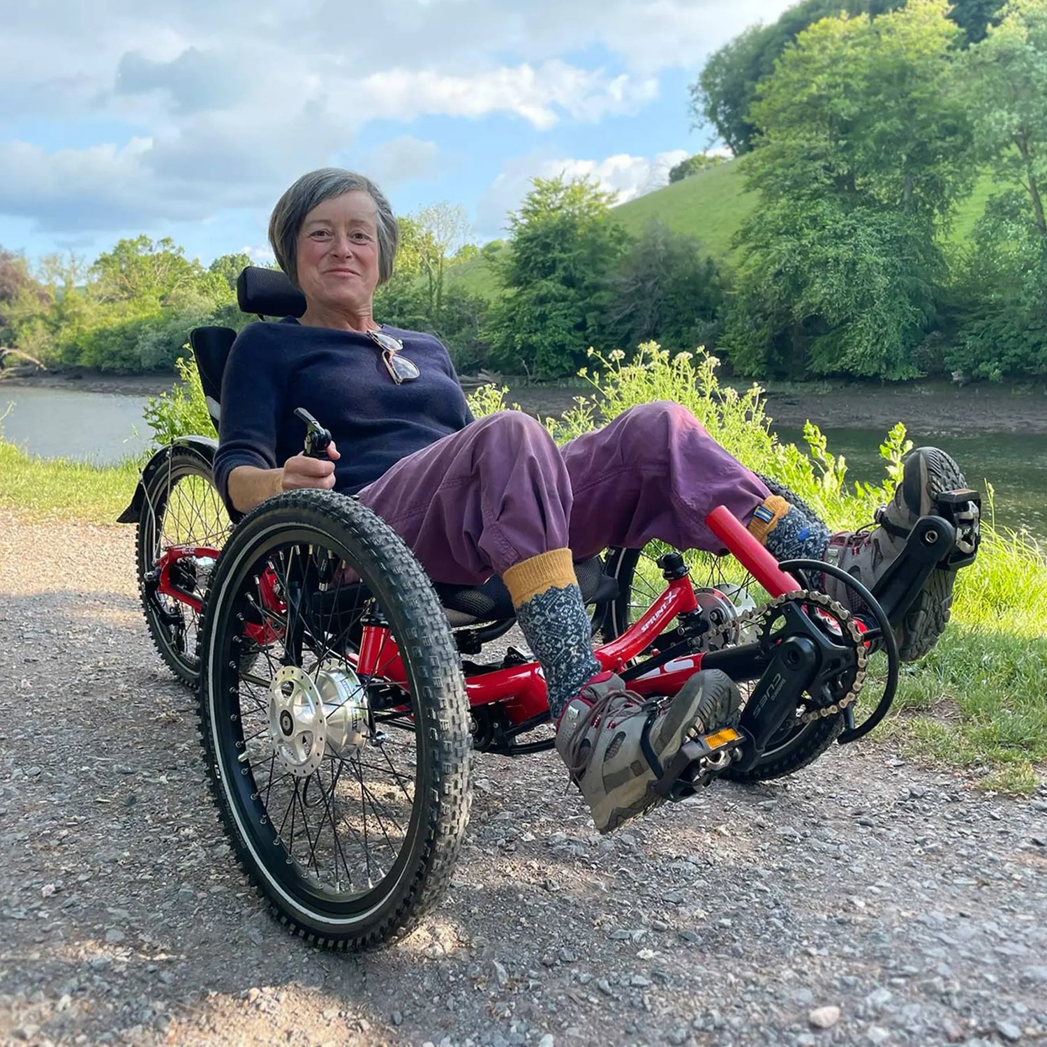 A woman rides an ICE Sprint Pixel on a gravel path along a wooded riverway.
