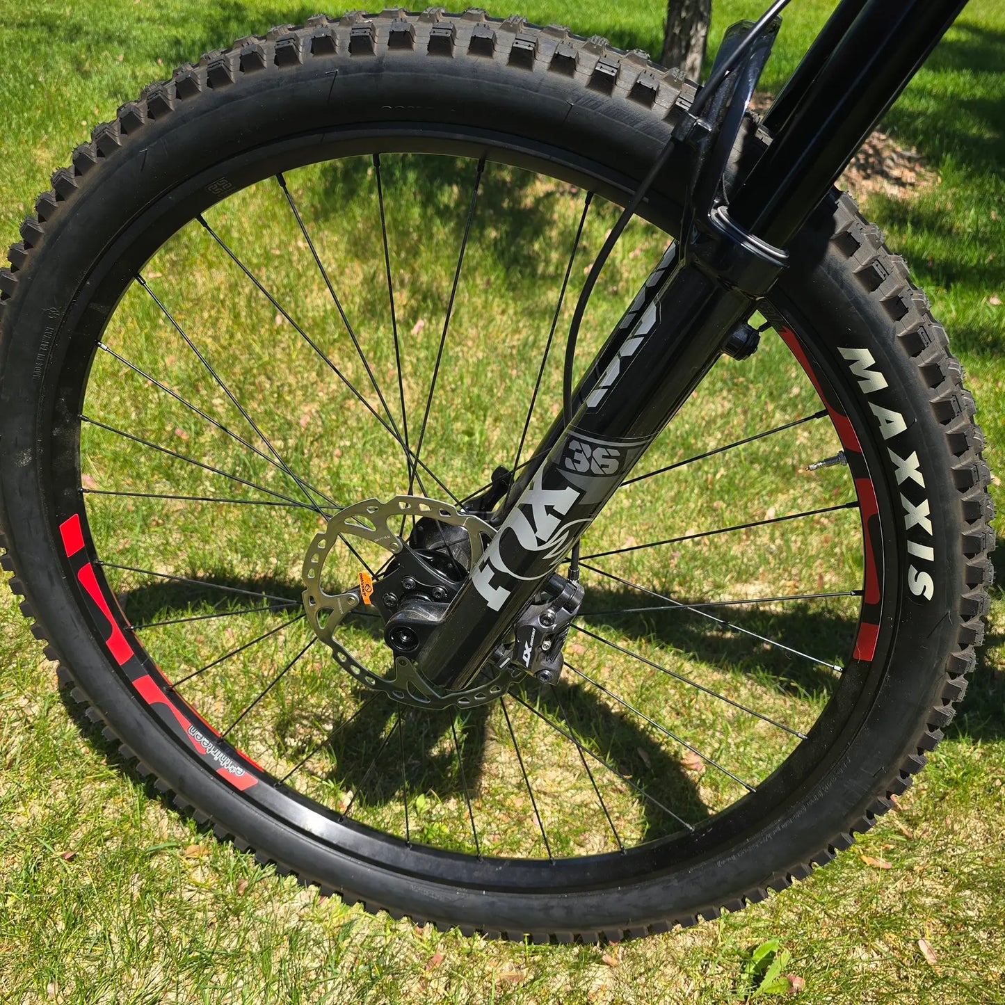 Closeup view of the front shock, disc brake and front wheel on the INTENSE Primer 29 Pro Midnight Grey-White in an outdoor setting.