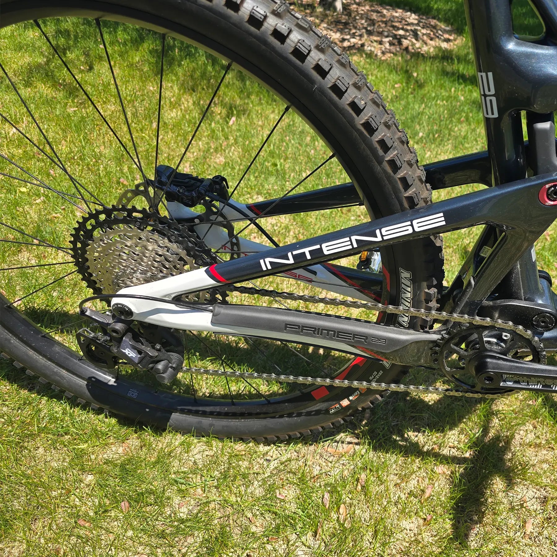 Closeup view of the rear frame, crankset, cassette and derailleur on the INTENSE Primer 29 Pro Midnight Grey-White in an outdoor setting.