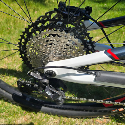 Closeup view of the rear derailleur and cassette on the INTENSE Primer 29 Pro Midnight Grey-White in an outdoor setting.