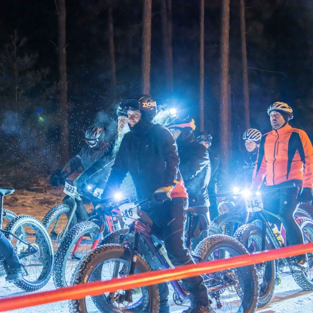 A group of several bikers stand together  on a snowy bike path waiting for the Iola Snow Bully Fat Bike Race to begin.