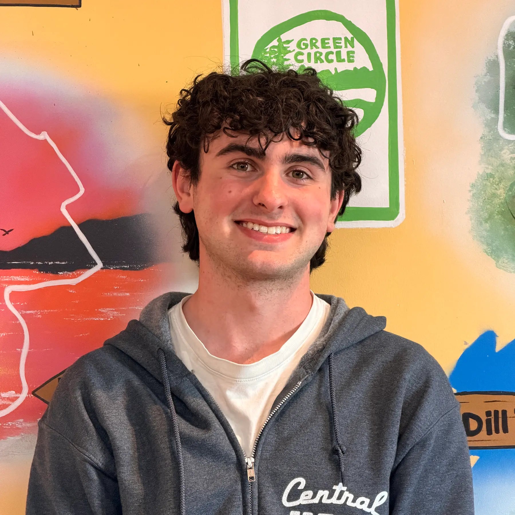 Jakob, Sales Staff member, in front of the Shoppe's Green Circle Mural, painted by KIBA Freeman Art: Muralist.