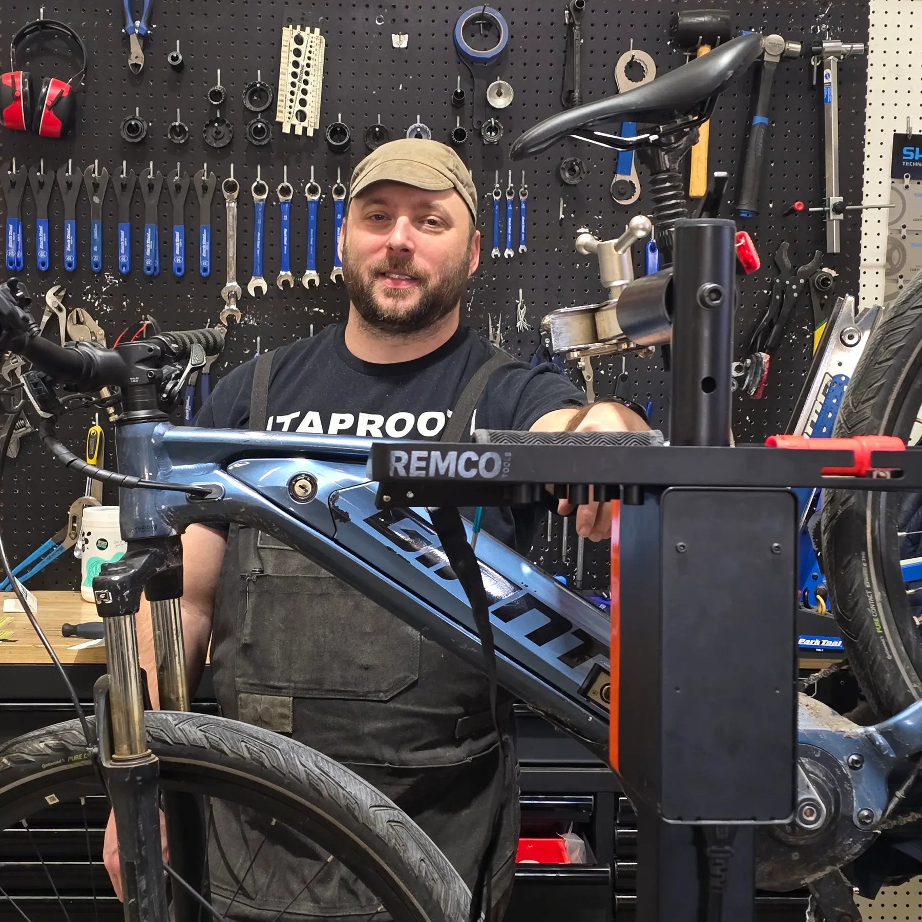 Man working on a bicycle in a workshop with tools and equipment on the wall.