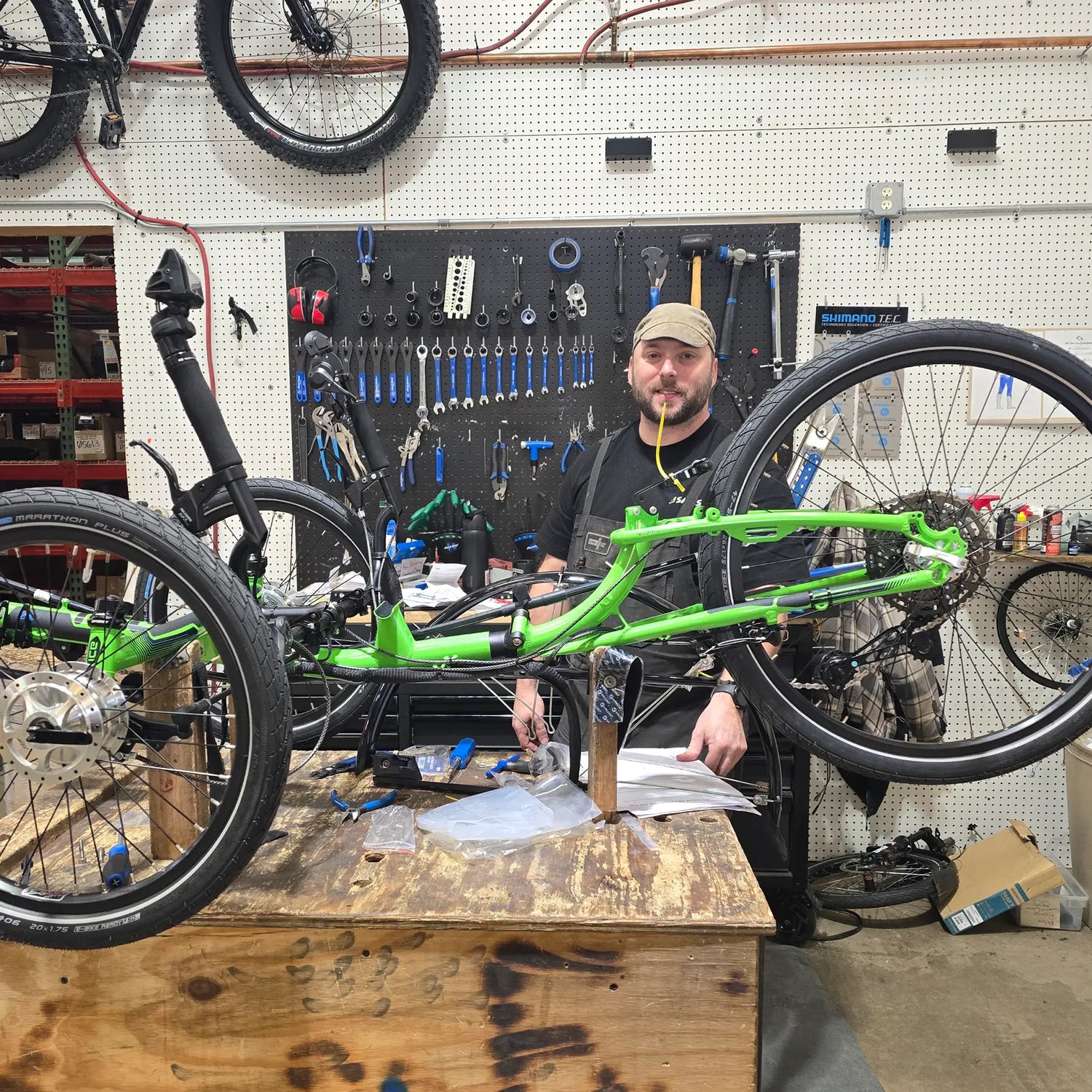 Man working on a green bicycle frame in a workshop with tools and equipment around.