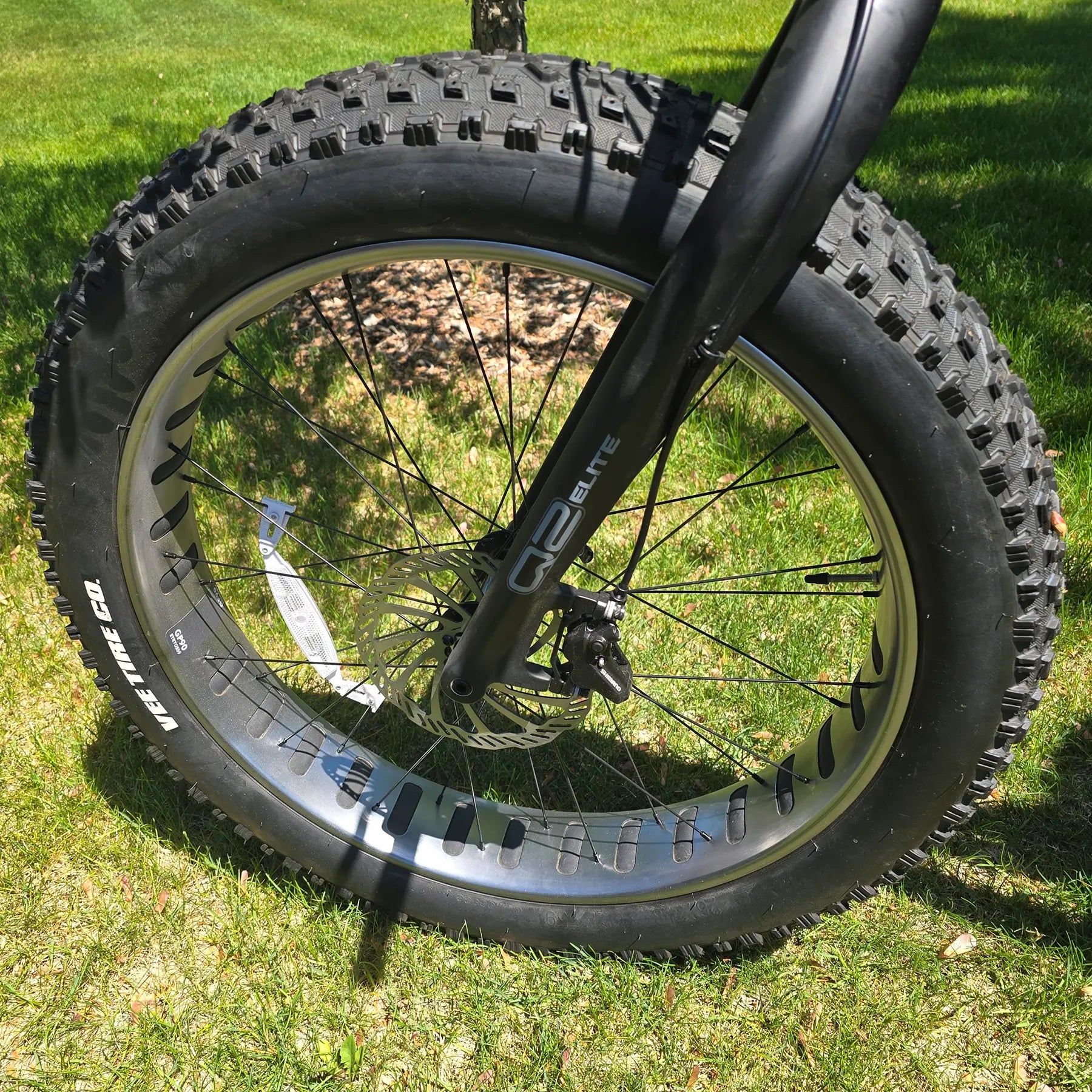 Closeup view of the fork, front wheel and brake on the KHS 4 Season 3000 Fat Bike with Carbon Fork in Black in an outdoor setting.