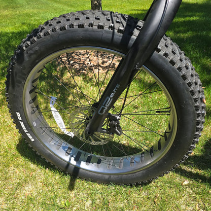 Closeup view of the fork, front wheel and brake on the KHS 4 Season 3000 Fat Bike with Carbon Fork in Black in an outdoor setting.