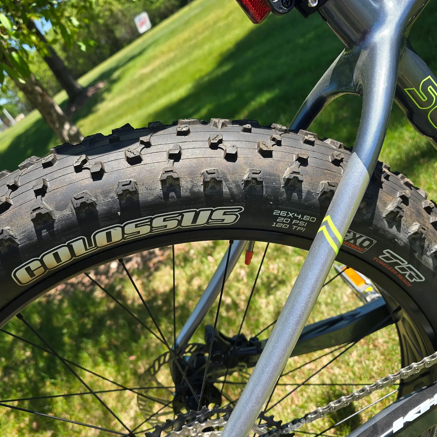 Closeup view of the rear tire and frame on the KHS 4 Season 5000 Fat Bike with Carbon Fork in Dark Grey in an outdoor setting.