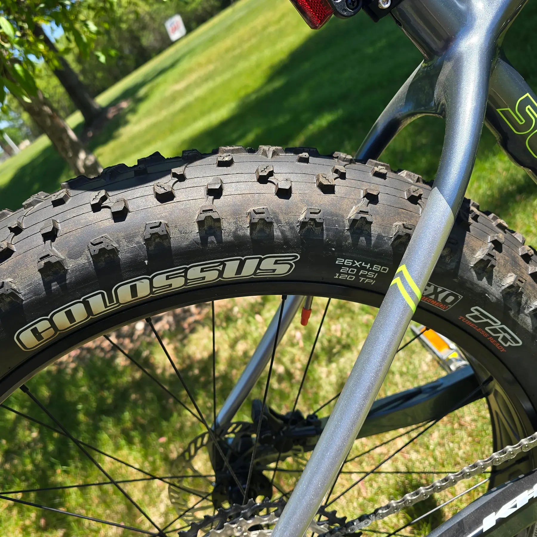 Closeup view of the rear tire and frame on the KHS 4 Season 5000 Fat Bike with Carbon Fork in Dark Grey in an outdoor setting.
