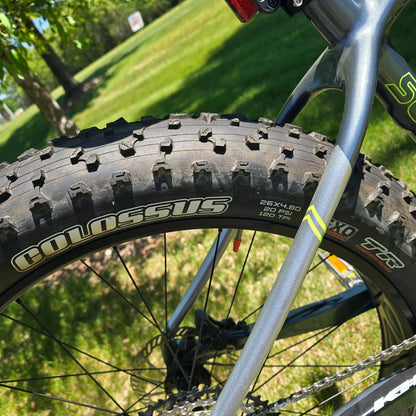 Closeup view of the rear tire and frame on the KHS 4 Season 5000 Fat Bike with Carbon Fork in Dark Grey in an outdoor setting.