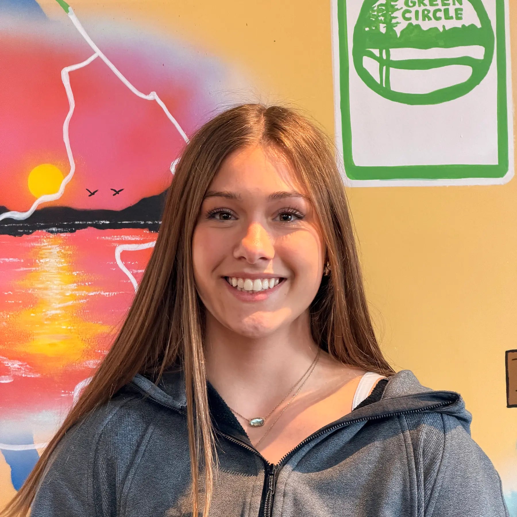 Lila, Sales Staff member, in front of the Shoppe's Green Circle Mural, painted by KIBA Freeman Art: Muralist.