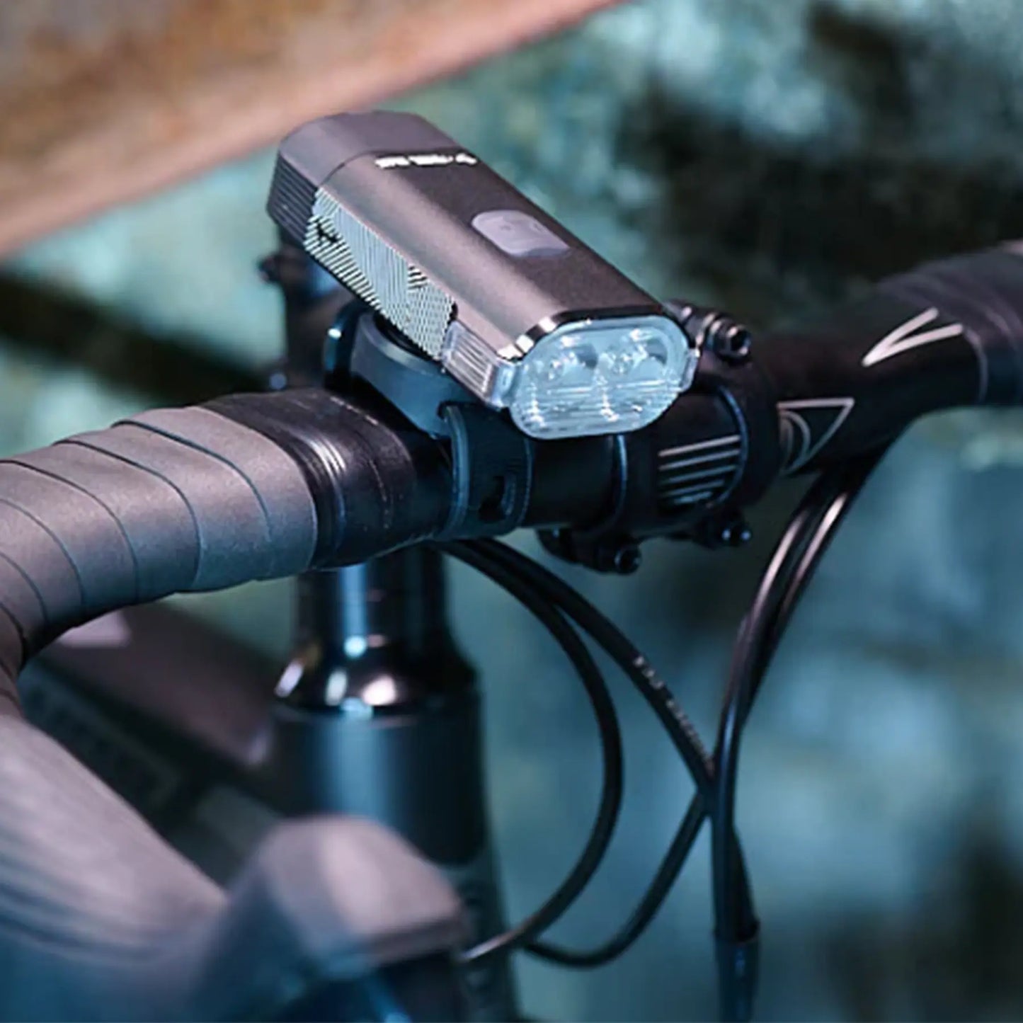 Image of the Moon Rigel Max 1500 Lumen Headlight in black mounted on a bike handlebar against a blurry blue background.