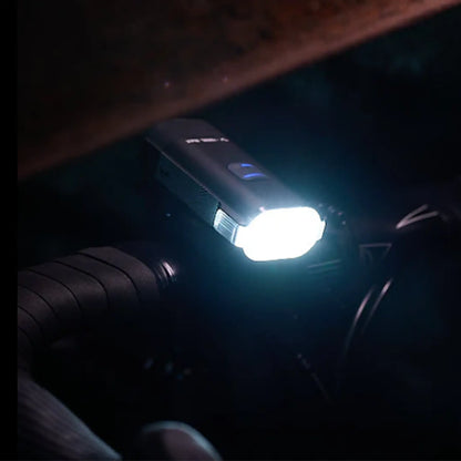 Image of the Moon Rigel Max 1500 Lumen Headlight in black turned on mounted on a bike handlebar against a nighttime background.