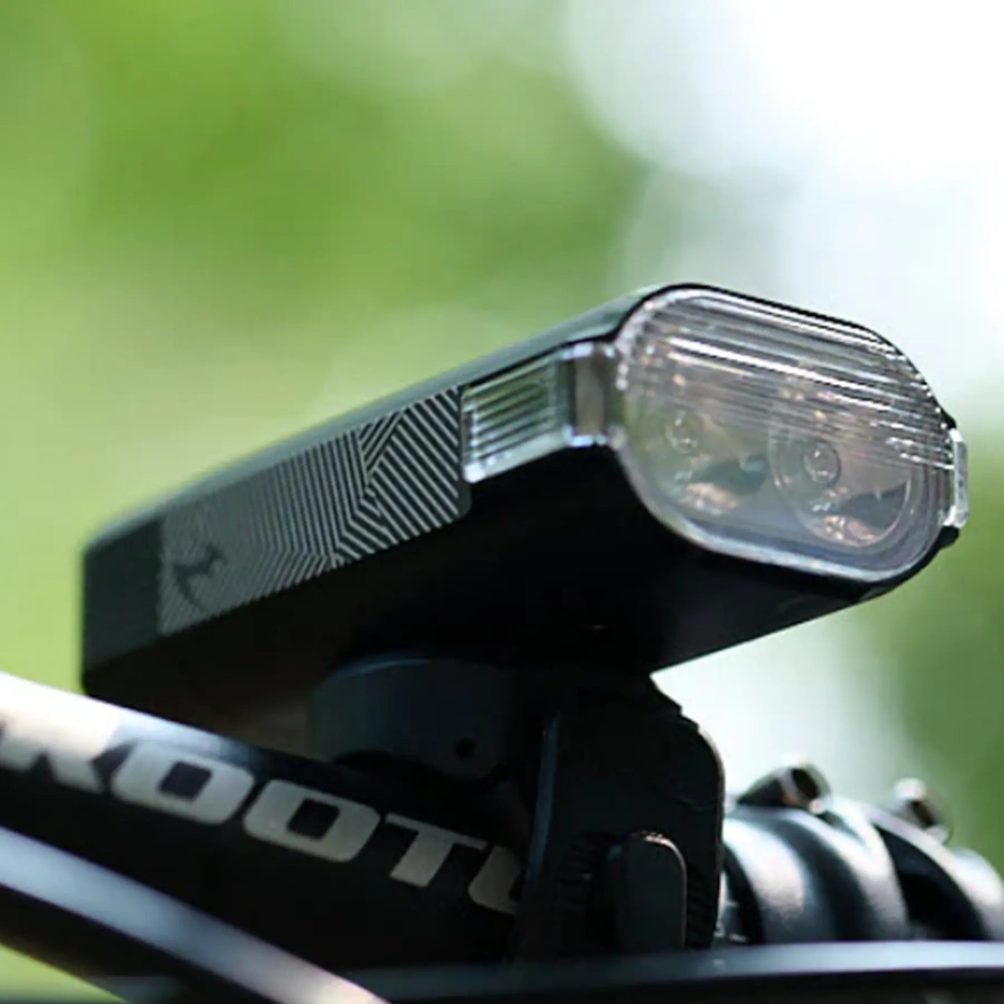 Image of the Moon Rigel Max 1500 Lumen Headlight in black mounted on a bike handlebar against a blurry green background.