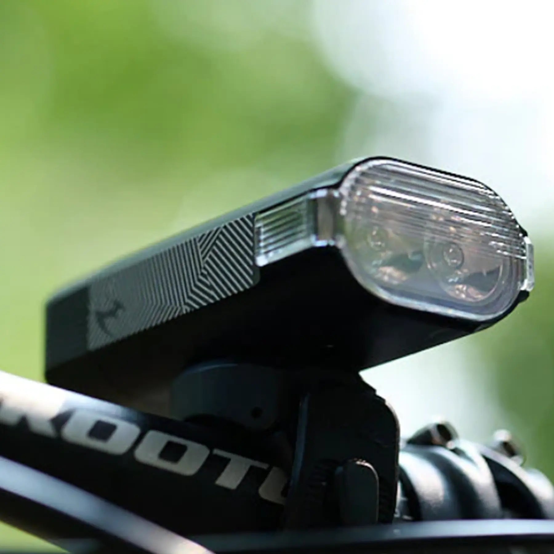 Image of the Moon Rigel Max 1500 Lumen Headlight in black mounted on a bike handlebar against a blurry green background.