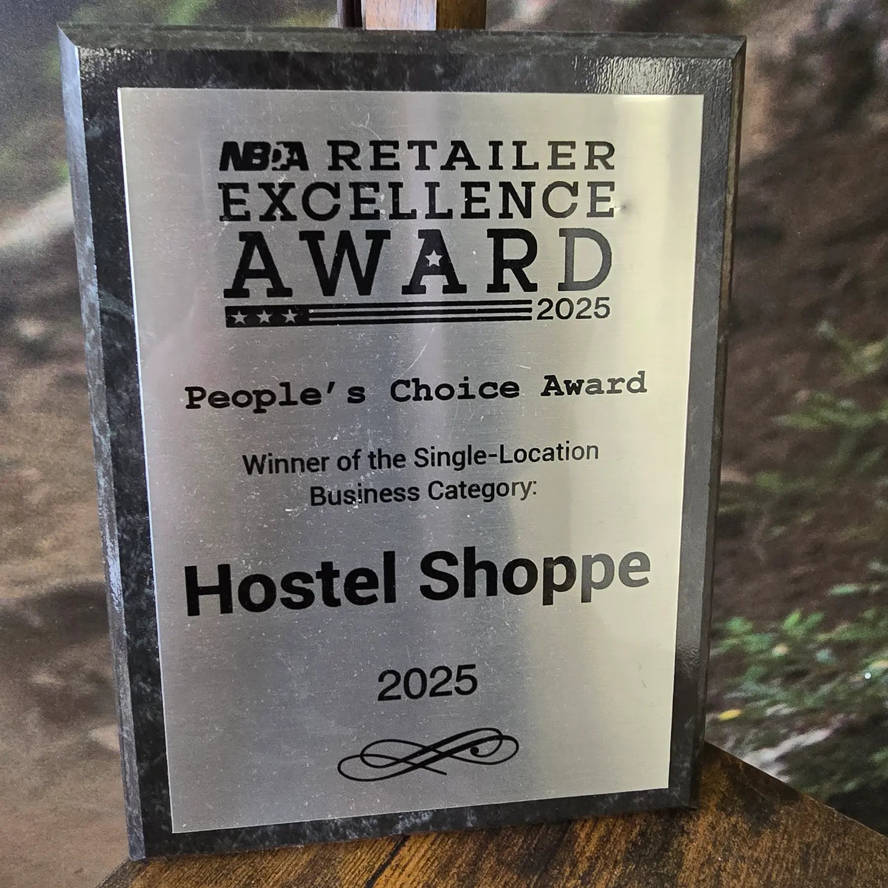 NBDA Retailer Excellence Award plaque for Hostel Shoppe in 2025 on a wooden surface with a blurred background.