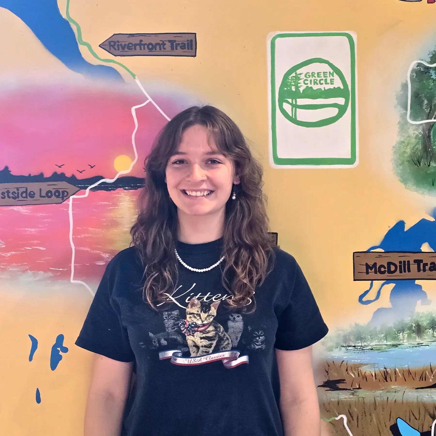 Neviah, Sales Staff member, in front of the Shoppe's Green Circle Mural, painted by KIBA Freeman Art: Muralist.