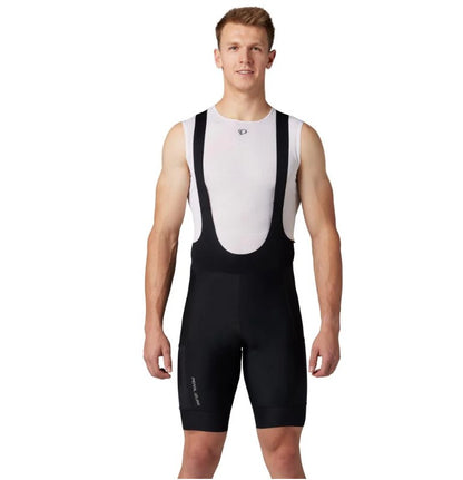 Man wearing black Pearl Izumi Expedition cycling bibs over a white tank top. 