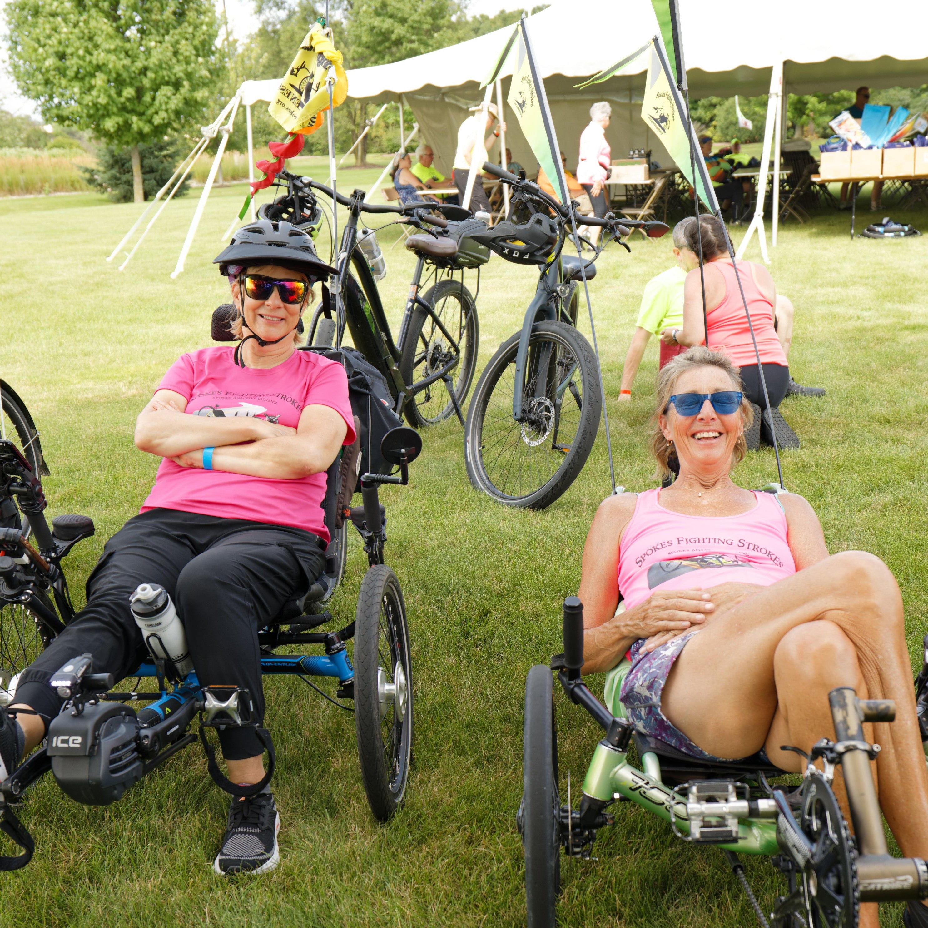 Two women are smiling and sitting on recumbent trikes in the grass at the Pedal Point Rally.
