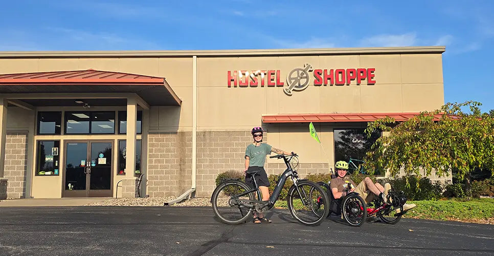 A woman and a man on a bike and trike in front of the Hostel Shoppe.