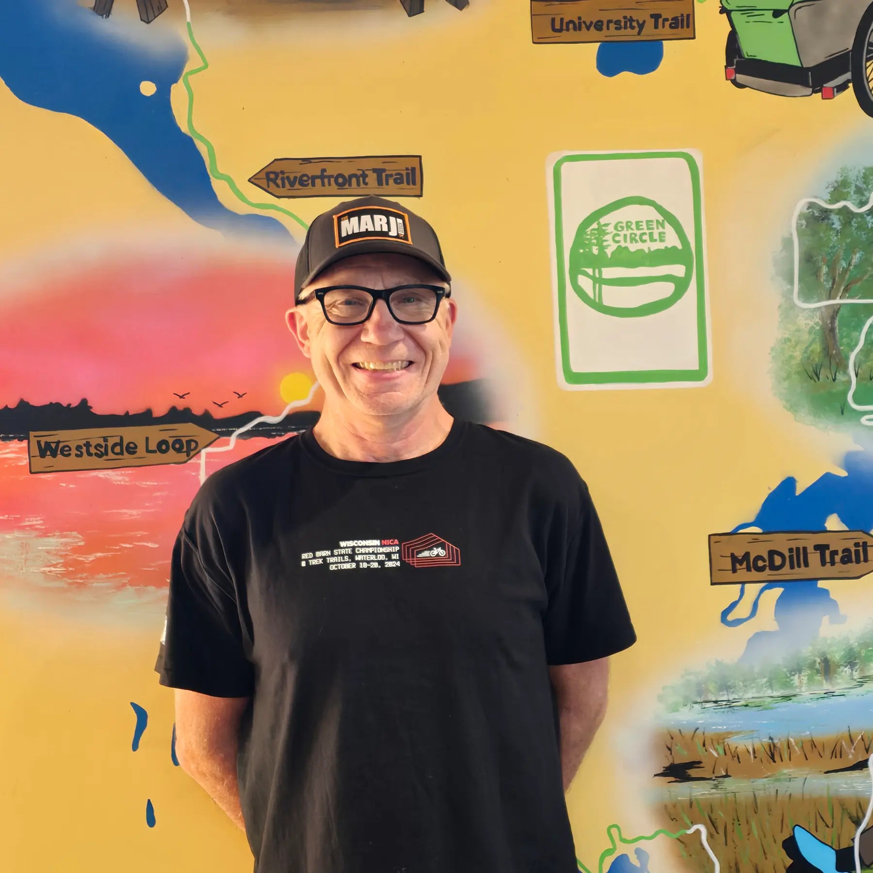Scott, Hostel Shoppe General Manager, in front of the Shoppe's Green Circle Mural, painted by KIBA Freeman Art: Muralist.