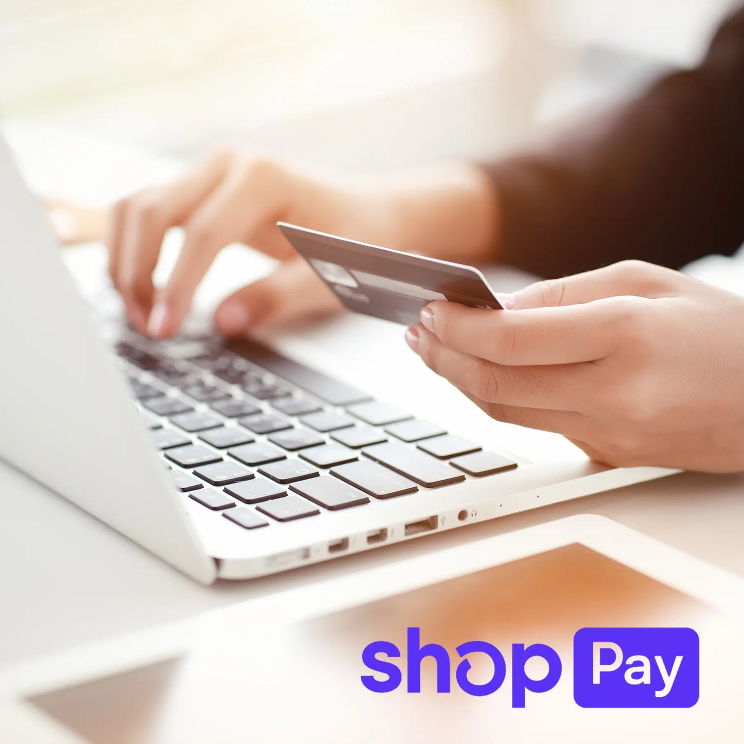 Person using a laptop with a credit card, blurred background with ShopPay logo.