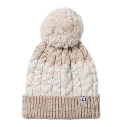 A cable-knit winter Smartwool Isto Retro Beanie with a fluffy pom-pom in Prosecco, featuring a color-blocked design in cream, light pink, and beige, finished with a ribbed knit cuff and a small brand tag.