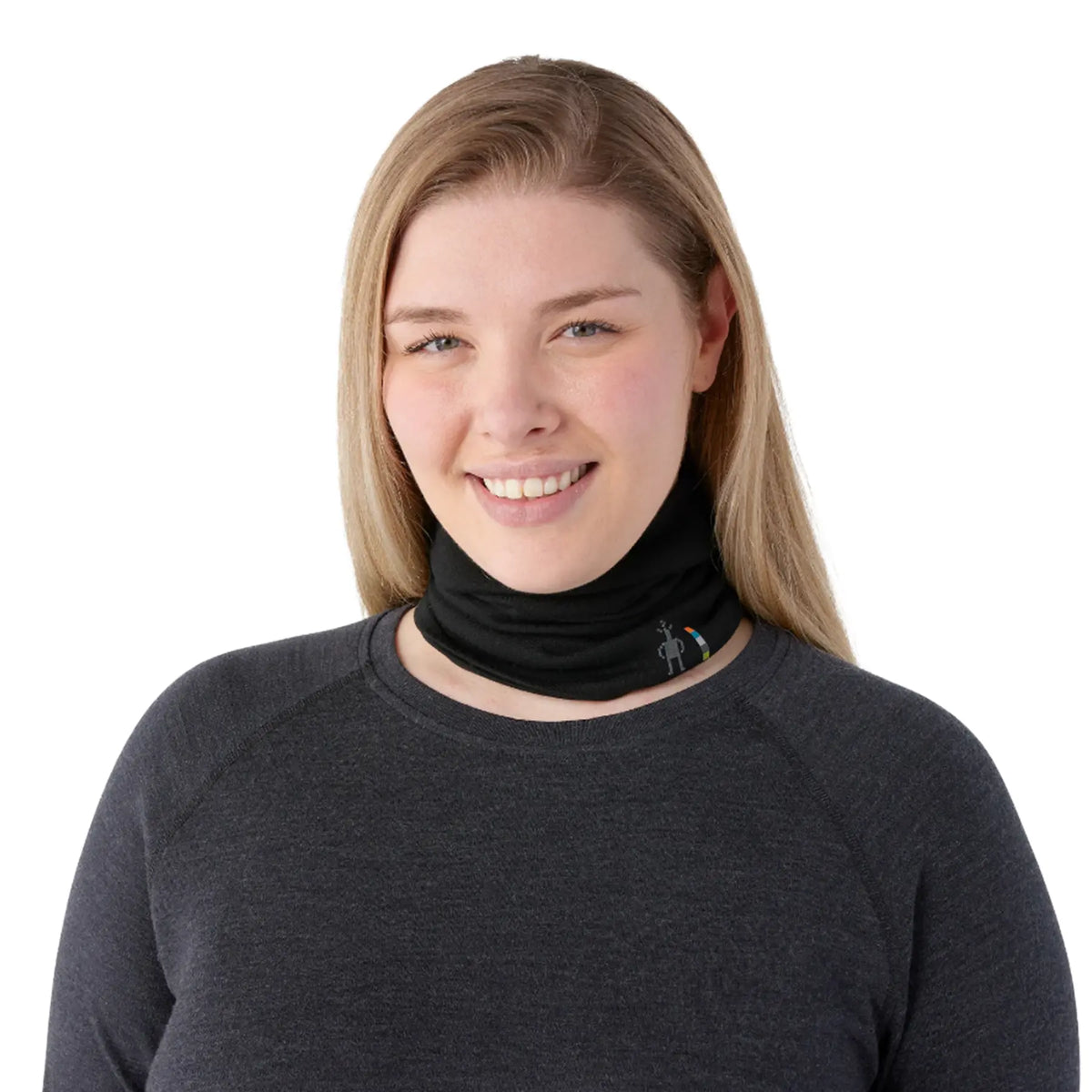 A smiling woman with blonde hair wearing a Smartwool Thermal Merino Reversible Neck Gaiter in black and a dark gray long-sleeve shirt, photographed against a solid white background.