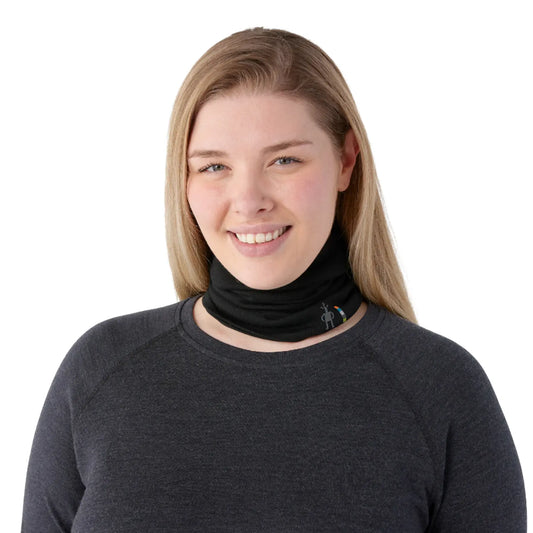 A smiling woman with blonde hair wearing a Smartwool Thermal Merino Reversible Neck Gaiter in black and a dark gray long-sleeve shirt, photographed against a solid white background.