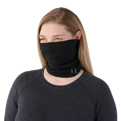 A woman wearing a Smartwool Thermal Merino Reversible Neck Gaiter in black pulled up below her nose, paired with a dark gray long-sleeve shirt, against a plain white background.