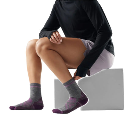 View of a woman on a bench trying on the Smartwool Womens Hike Full Cushion Crew Socks Medium Gray with pink and purple accents against a white background.