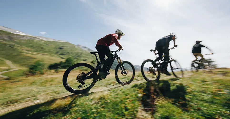 Three people riding Specialized mountain bikes on a trail with a clear sky.