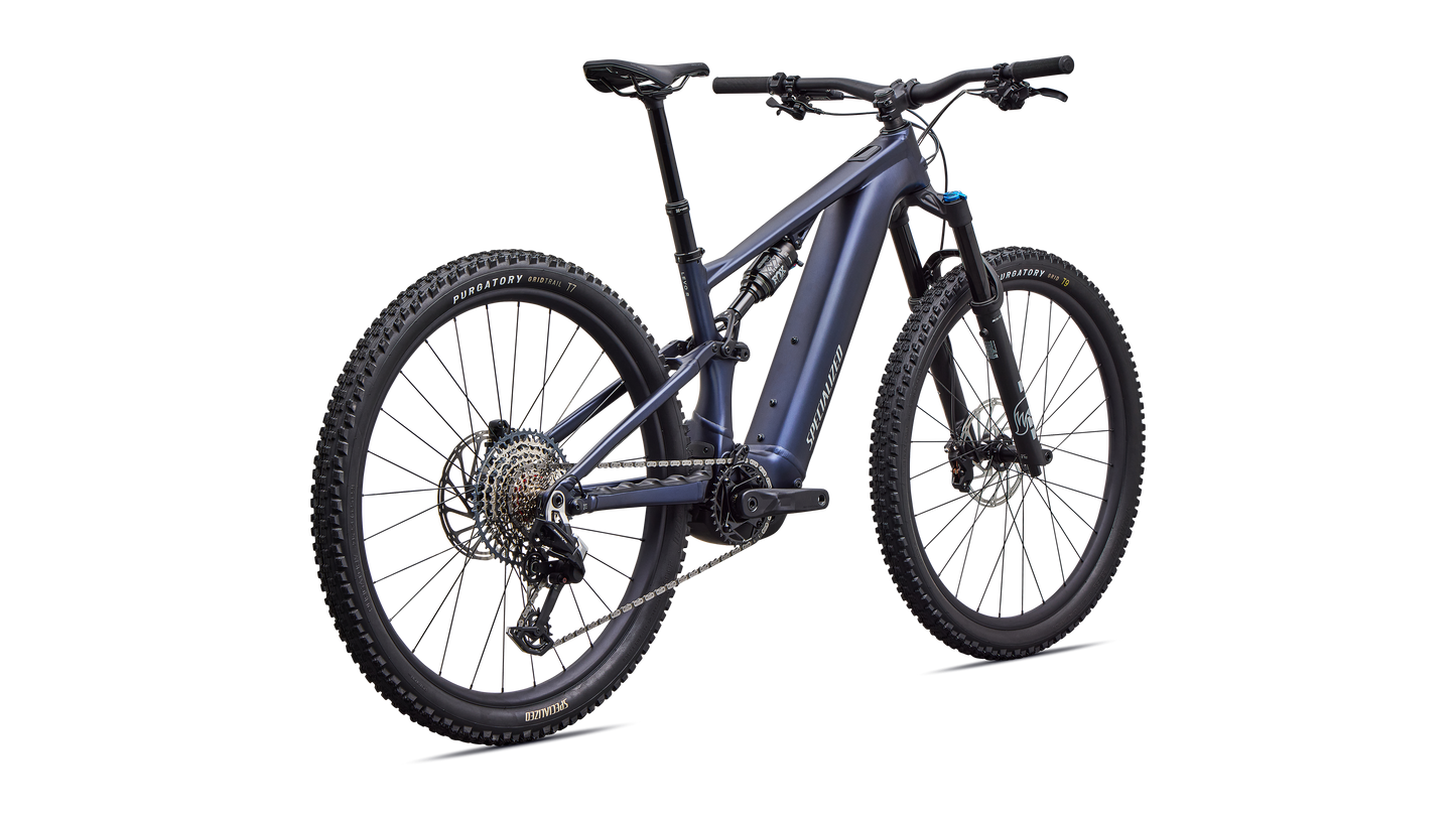 A full-suspension electric mountain bike in a dark metallic blue-gray color, featuring a black battery pack, front suspension fork, and knobby tires, shown on a solid white background.