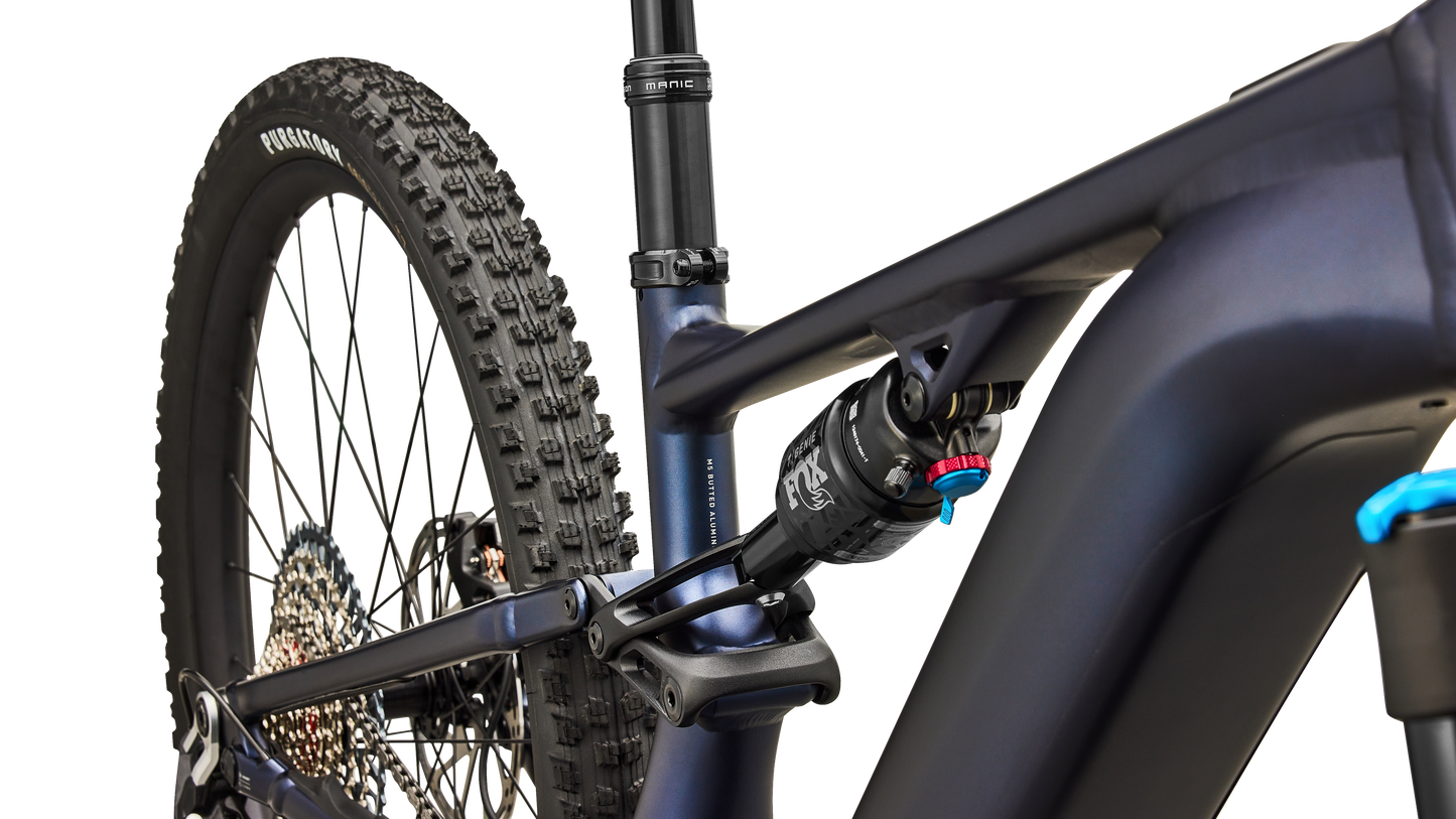 Close-up rear view of a matte navy blue mountain bike frame with a rear suspension fork, rear tire, and drivetrain components on a clean white background.