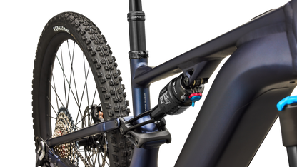 Close-up rear view of a matte navy blue mountain bike frame with a rear suspension fork, rear tire, and drivetrain components on a clean white background.