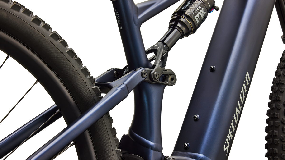 Close-up of a Specialized mountain bike frame in matte navy blue, showing the seat tube junction, rear shock, and part of the rear tire against a clean white background.