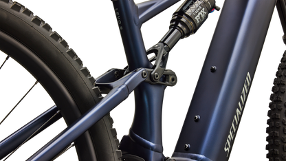 Close-up of a Specialized mountain bike frame in matte navy blue, showing the seat tube junction, rear shock, and part of the rear tire against a clean white background.