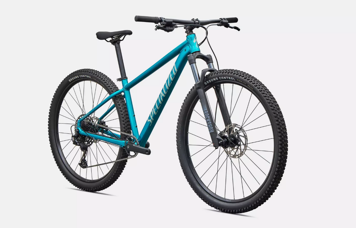 A front angled view of a teal Specialized Rockhopper Comp with black tires, seat post and seat, on a white background.