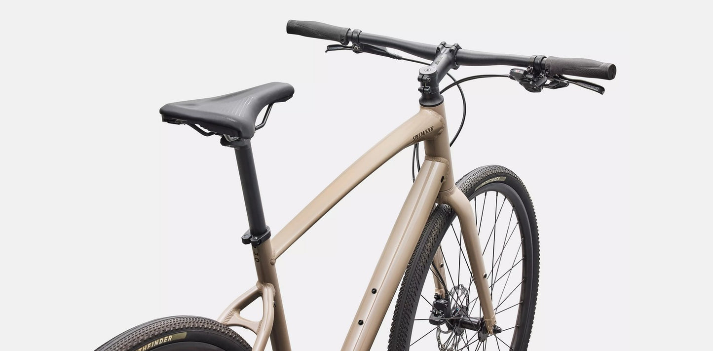 Closer view of saddle and handlebars of a beige Specialized Sirrus bicycle with black components on a white background. 