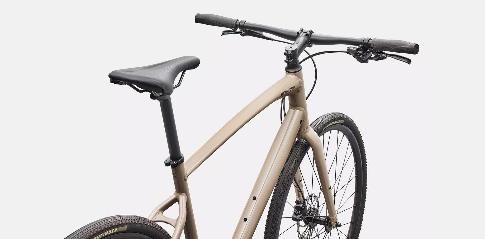 Closer view of saddle and handlebars of a beige Specialized Sirrus bicycle with black components on a white background. 