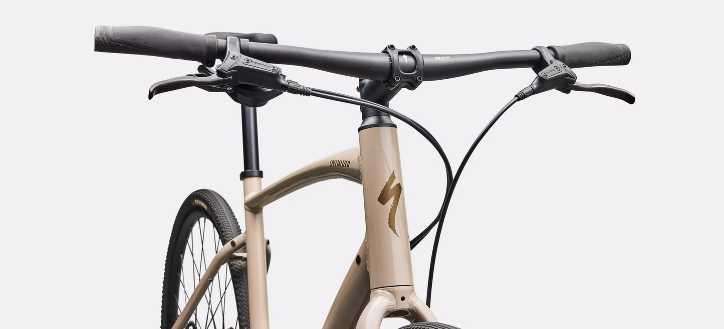 Close-up of a bicycle handlebar and frame of a beige Specialized Sirrus bicycle with black components on a white background.