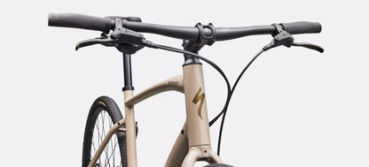 Close-up of a bicycle handlebar and frame of a beige Specialized Sirrus bicycle with black components on a white background.