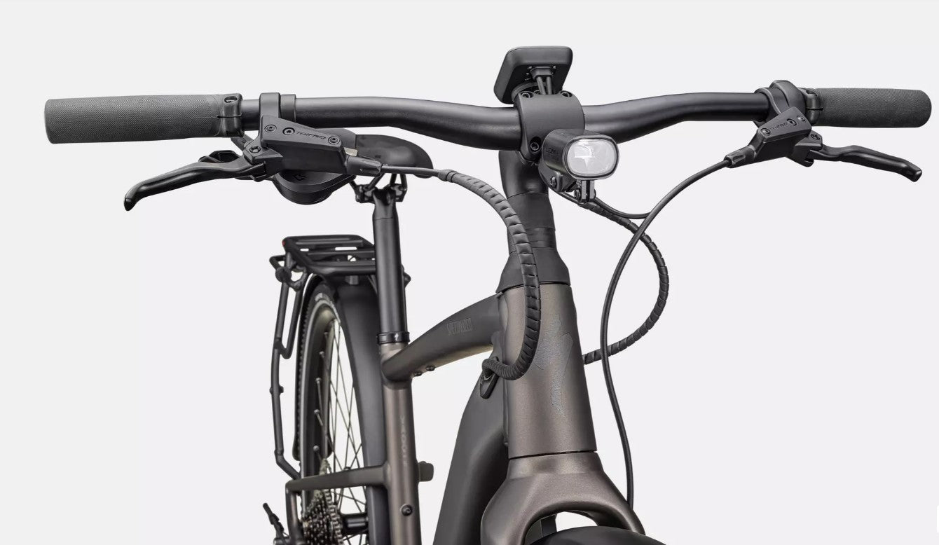 Close-up of a bicycle handlebar and front wheel of a dark grey Specialized Vado SL electric bicycle on a white background
