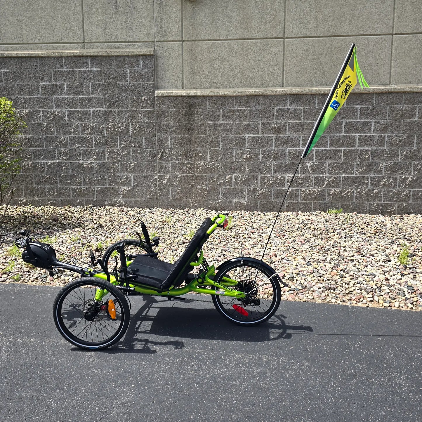 View of the Spokes Fighting Strokes Logo Flag with Handicapped Symbol  on a trike in an outdoor setting.