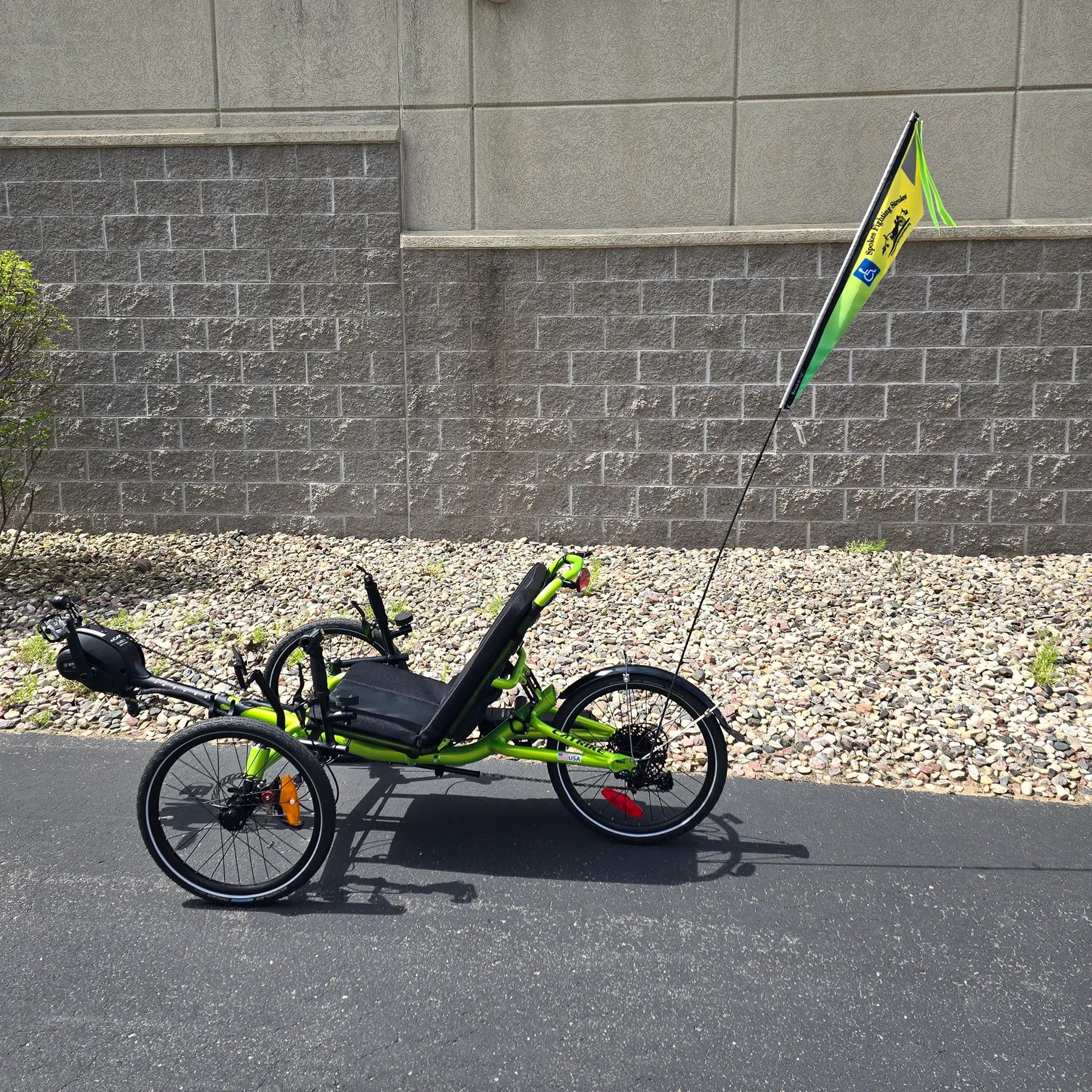 View of the Spokes Fighting Strokes Logo Flag with Handicapped Symbol  on a trike in an outdoor setting.
