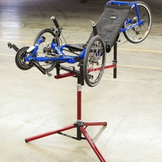 Blue recumbent trike on a red repair stand in an indoor setting.