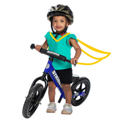 A toddler female sits on a blue Strider balance bike.
