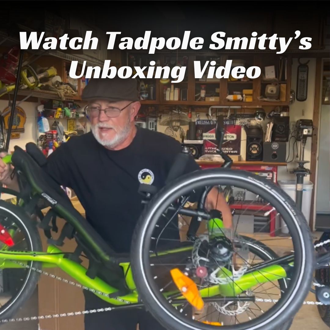 A man carries a green trike with text overlay about watching his unboxing video.